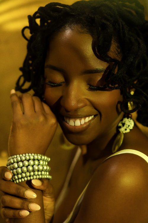 Woman with braided hair and green bracelets smiling against a warm-toned background