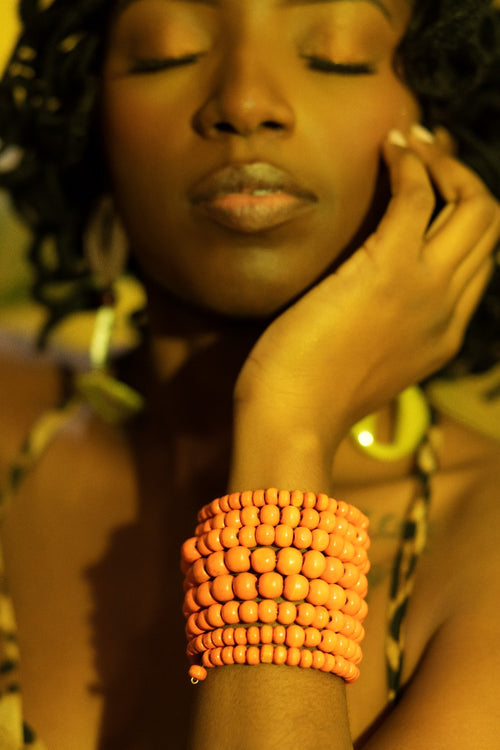 Woman with a large orange beaded bracelet on her wrist, wearing gold jewelry.